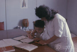 Mujer junto a niño pequeño en una mesa escribiendo