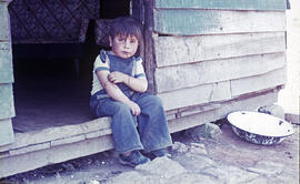 Niño sentado en la puerta de una casa